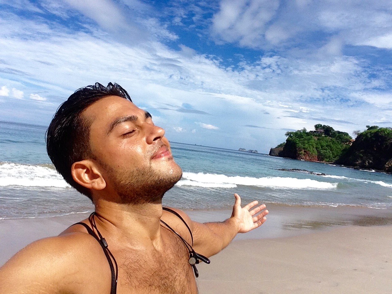Sean Ali standing on a tropical beach with arms open